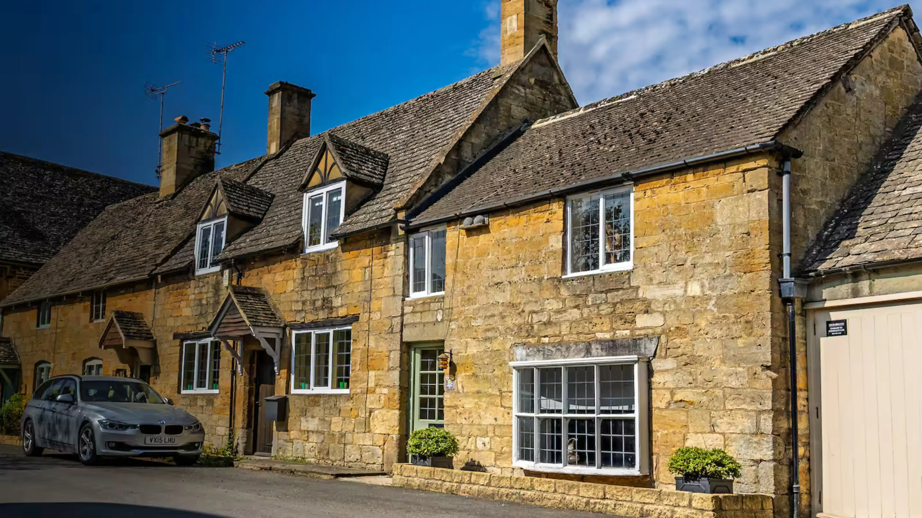 Golden stone holiday cottages on a sunny Cotswold street, managed as profitable short-lets